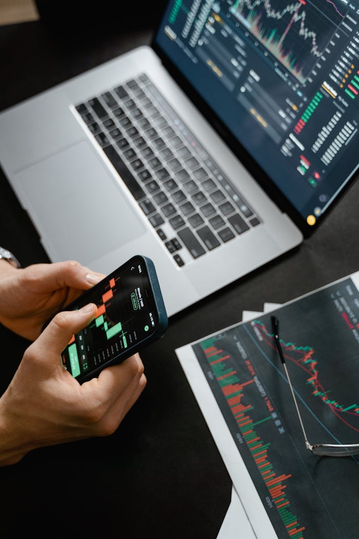 why-choose-us Hands holding phone with financial graph, laptop in view.